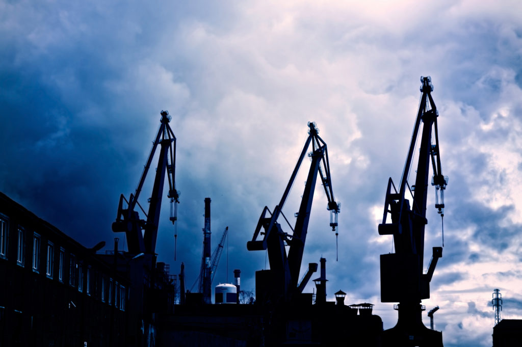 Industrial conceptual image. Dark and sullen clouds over industrial shipyard area with cranes.